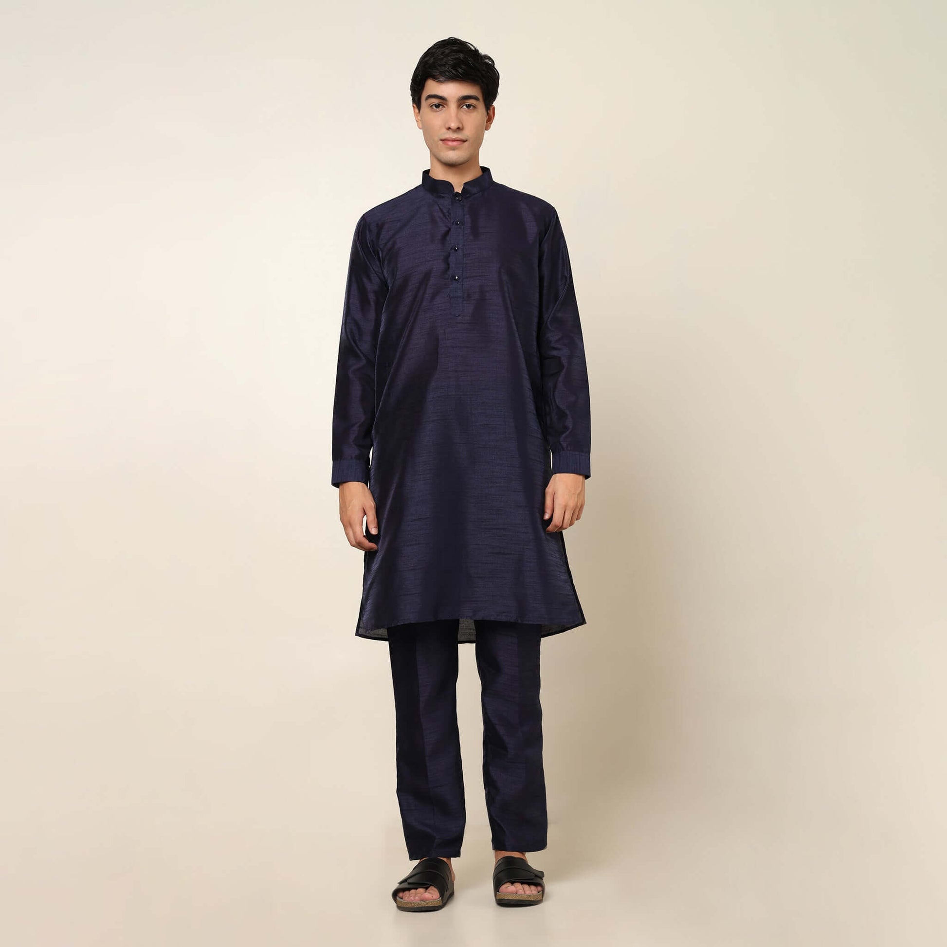 Model posing in evening blue kurta jacket set for men by Crease India, which is made up of dupion silk & has sequence embroidery design on jacket. Ideal for groom and guests at Indian wedding reception, engagement, sangeet, cocktail party, anniversary and