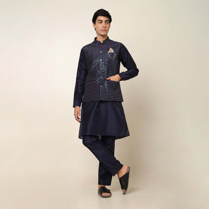 Model posing in evening blue kurta jacket set for men by Crease India, which is made up of dupion silk & has sequence embroidery design on jacket. Ideal for groom and guests at Indian wedding reception, engagement, sangeet, cocktail party, anniversary and