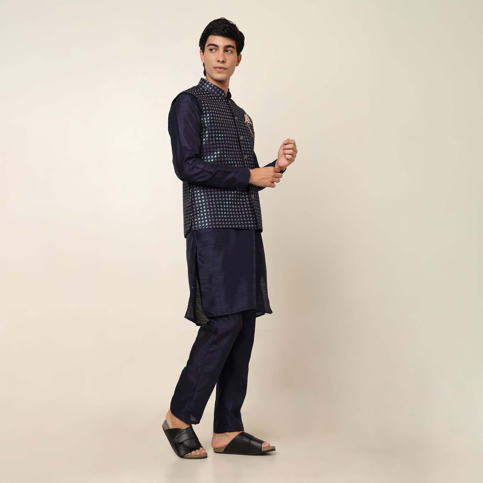 Model posing in evening blue kurta jacket set for men by Crease India, which is made up of dupion silk & has sequence embroidery design on jacket. Ideal for groom and guests at Indian wedding reception, engagement, sangeet, cocktail party, anniversary and