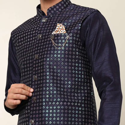 Model posing in evening blue kurta jacket set for men by Crease India, which is made up of dupion silk & has sequence embroidery design on jacket. Ideal for groom and guests at Indian wedding reception, engagement, sangeet, cocktail party, anniversary and