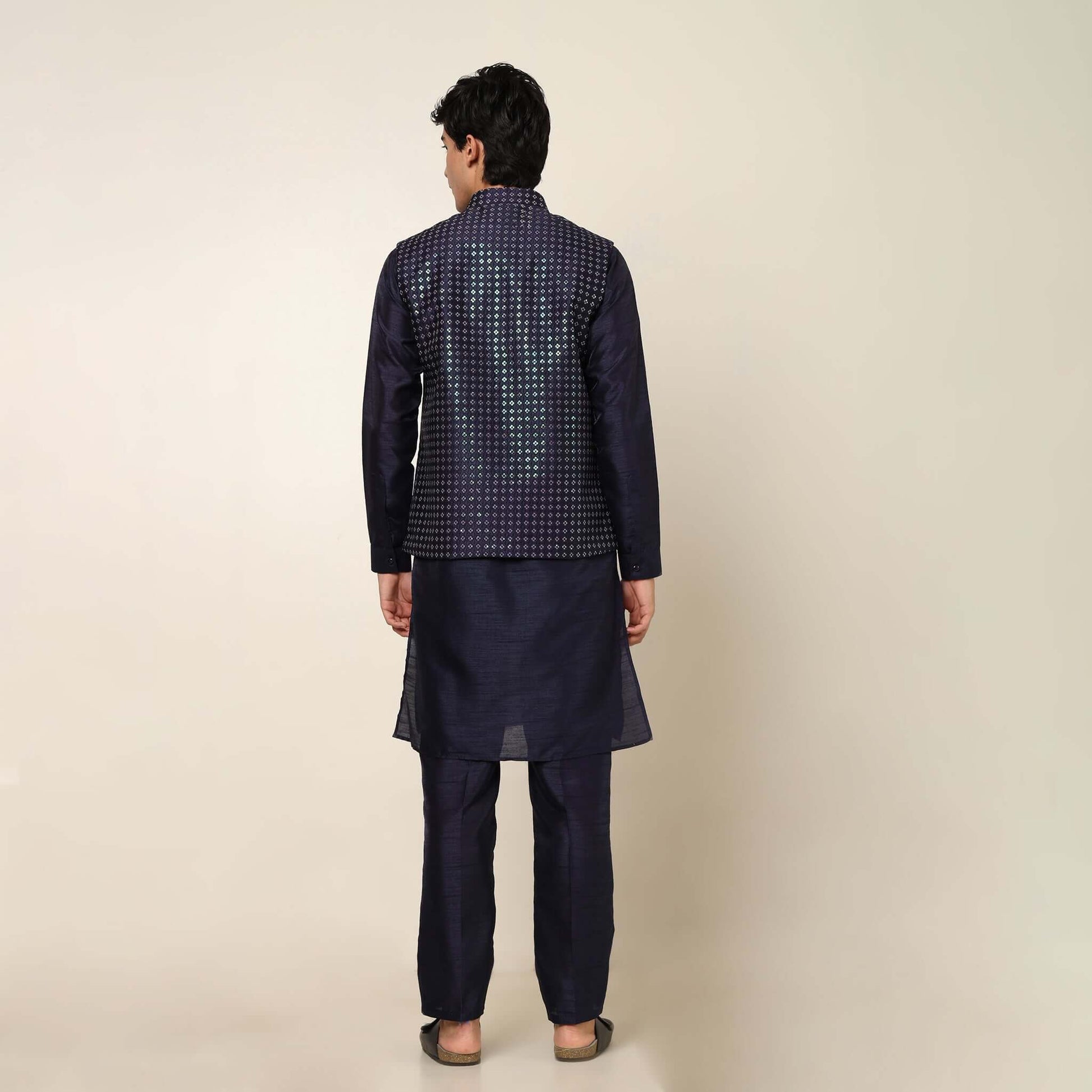 Model posing in evening blue kurta jacket set for men by Crease India, which is made up of dupion silk & has sequence embroidery design on jacket. Ideal for groom and guests at Indian wedding reception, engagement, sangeet, cocktail party, anniversary and