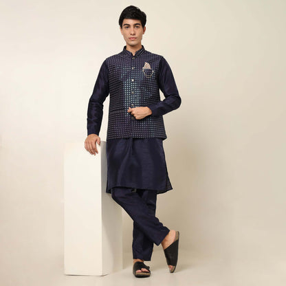 Model posing in evening blue kurta jacket set for men by Crease India, which is made up of dupion silk & has sequence embroidery design on jacket. Ideal for groom and guests at Indian wedding reception, engagement, sangeet, cocktail party, anniversary and