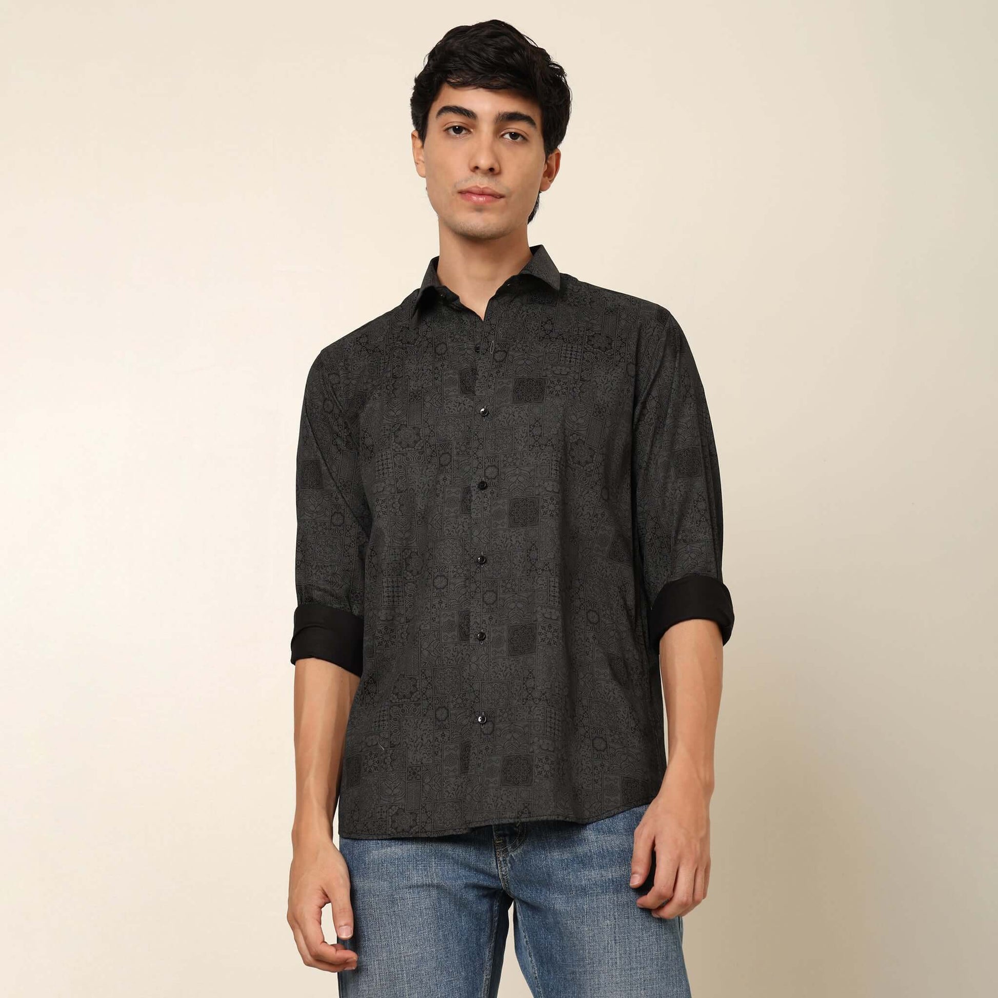 Model posing in regular fit printed black casual shirt for men by Crease India, made up of soft cotton satin fabric it has floral and geometric prints along with long sleeves. Perfect black shirt for men to wear it as party shirt, brunch shirt, after part