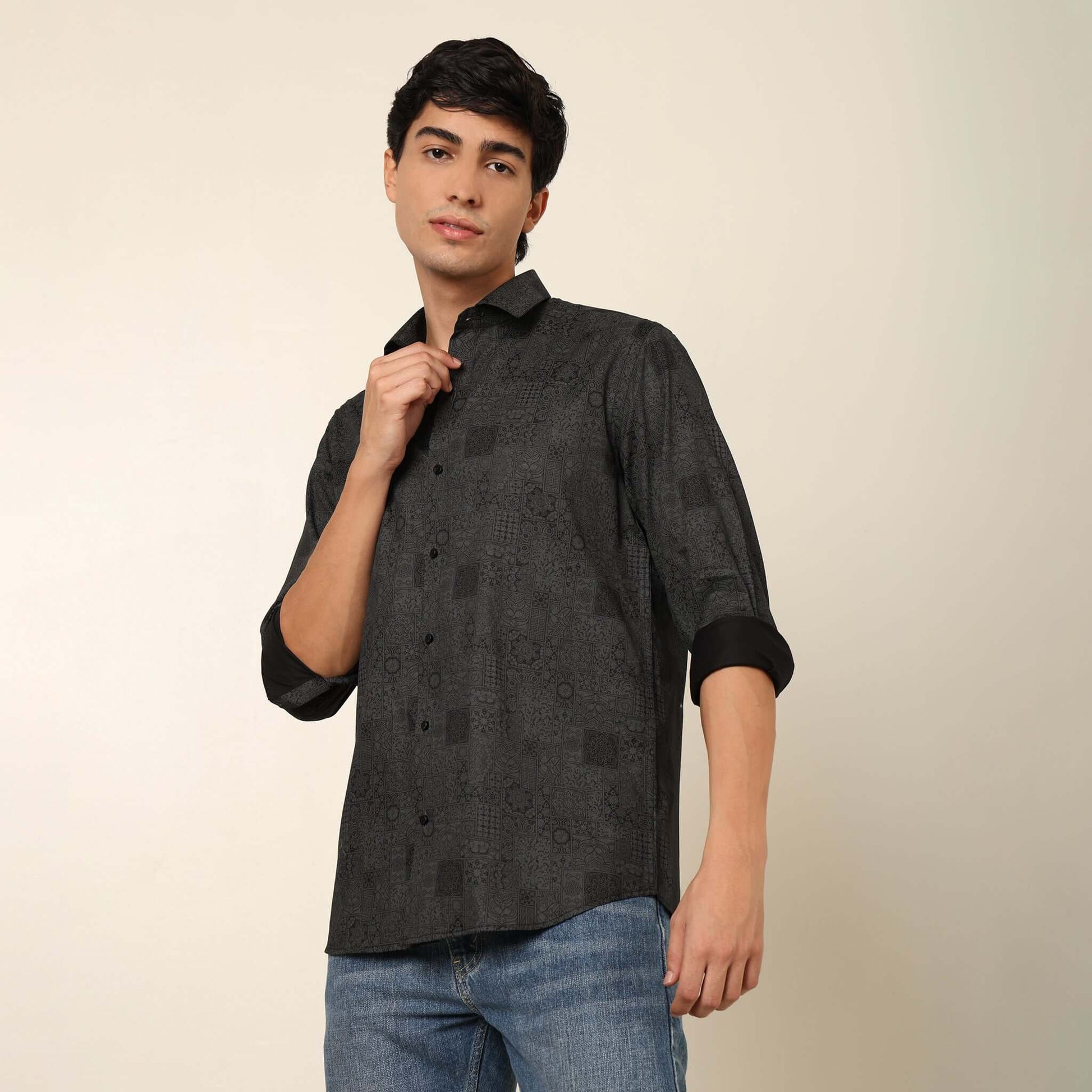 Model posing in regular fit printed black casual shirt for men by Crease India, made up of soft cotton satin fabric it has floral and geometric prints along with long sleeves. Perfect black shirt for men to wear it as party shirt, brunch shirt, after part