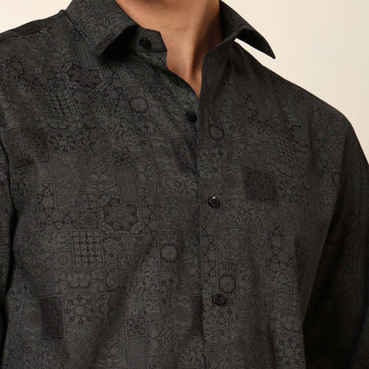 Model posing in regular fit printed black casual shirt for men by Crease India, made up of soft cotton satin fabric it has floral and geometric prints along with long sleeves. Perfect black shirt for men to wear it as party shirt, brunch shirt, after part