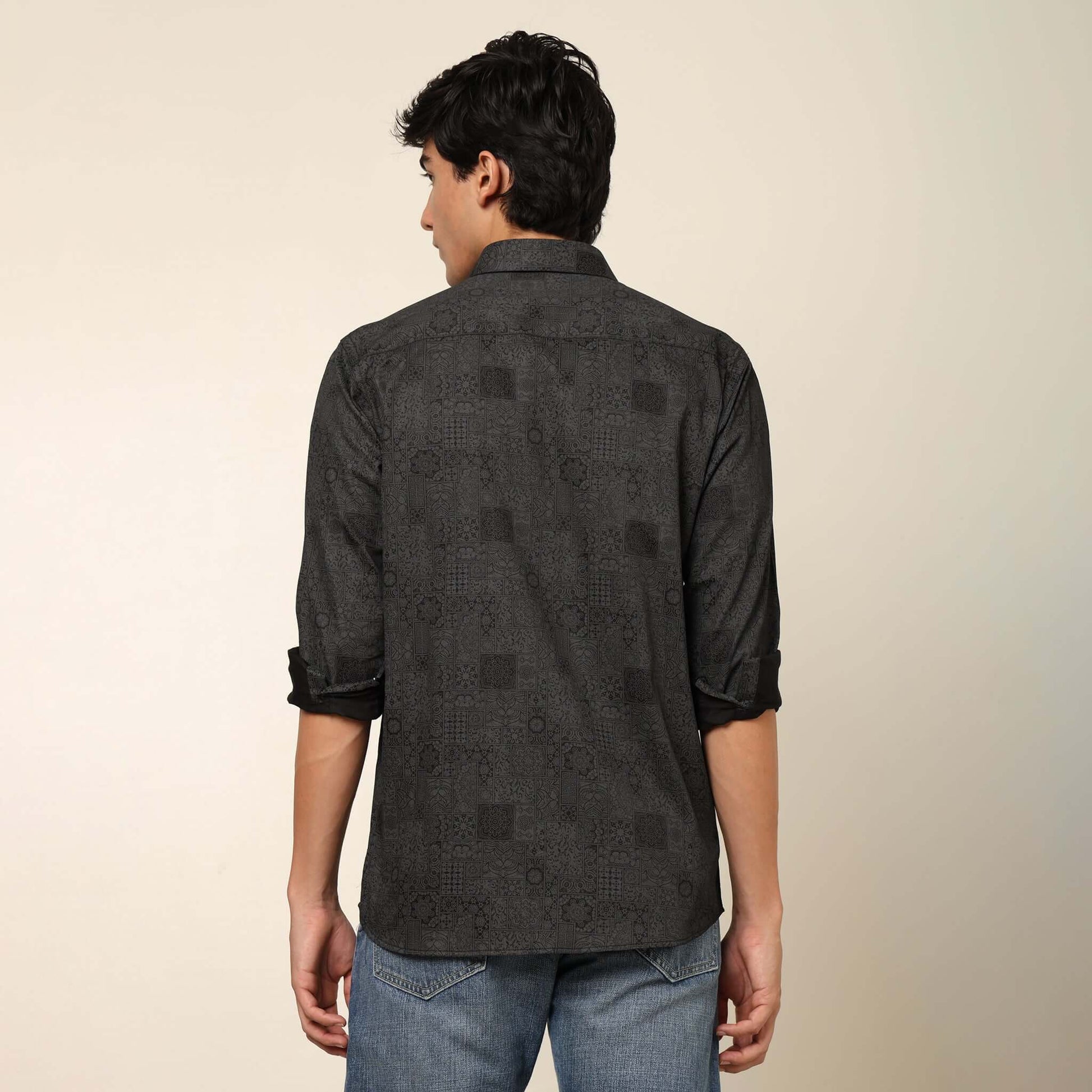 Model posing in regular fit printed black casual shirt for men by Crease India, made up of soft cotton satin fabric it has floral and geometric prints along with long sleeves. Perfect black shirt for men to wear it as party shirt, brunch shirt, after part