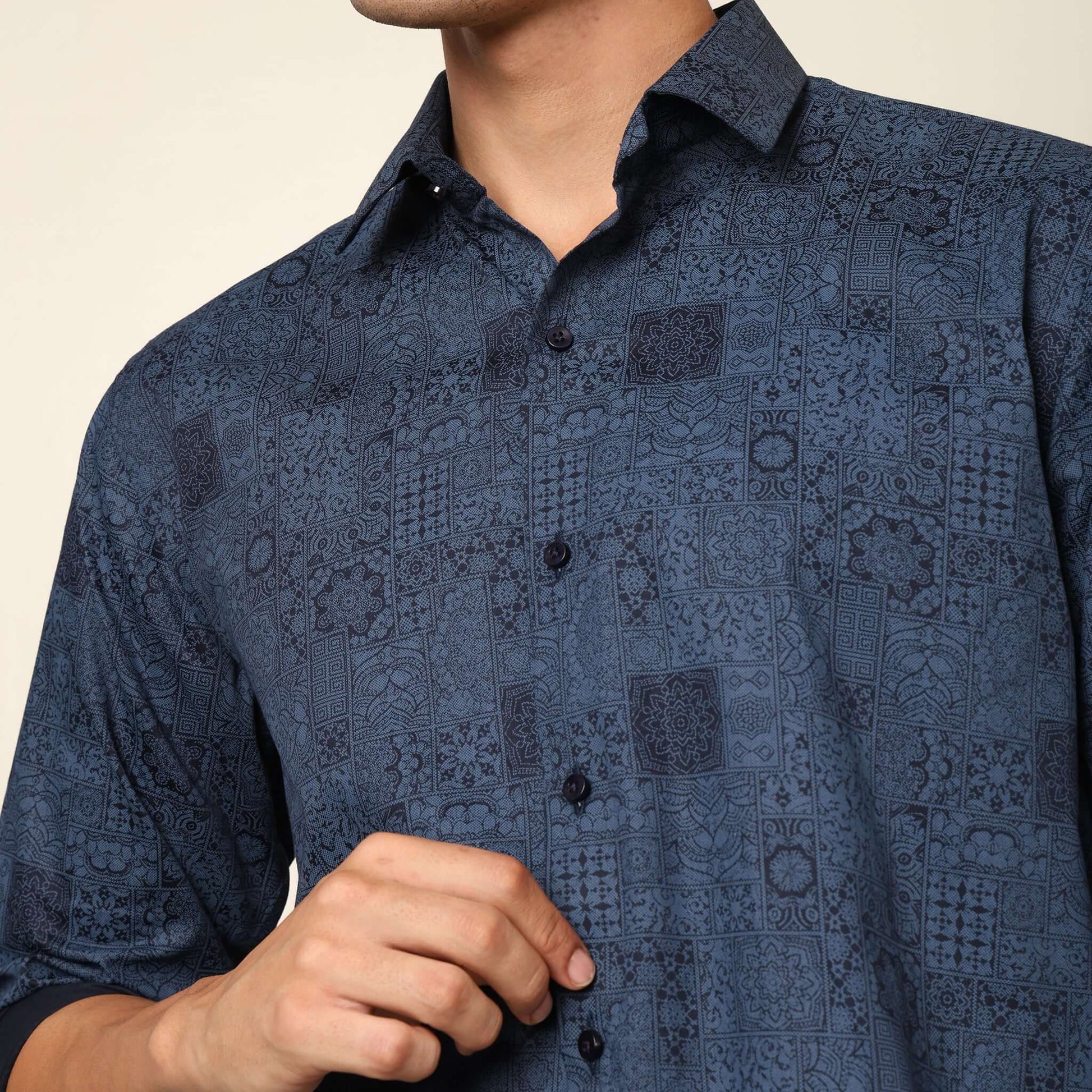 Model posing in regular fit printed blue casual shirt for men by Crease India, made up of soft cotton satin fabric it has floral and geometric prints along with long sleeves. Perfect for men to wear it as party shirt, brunch shirt, after party shirt, casu