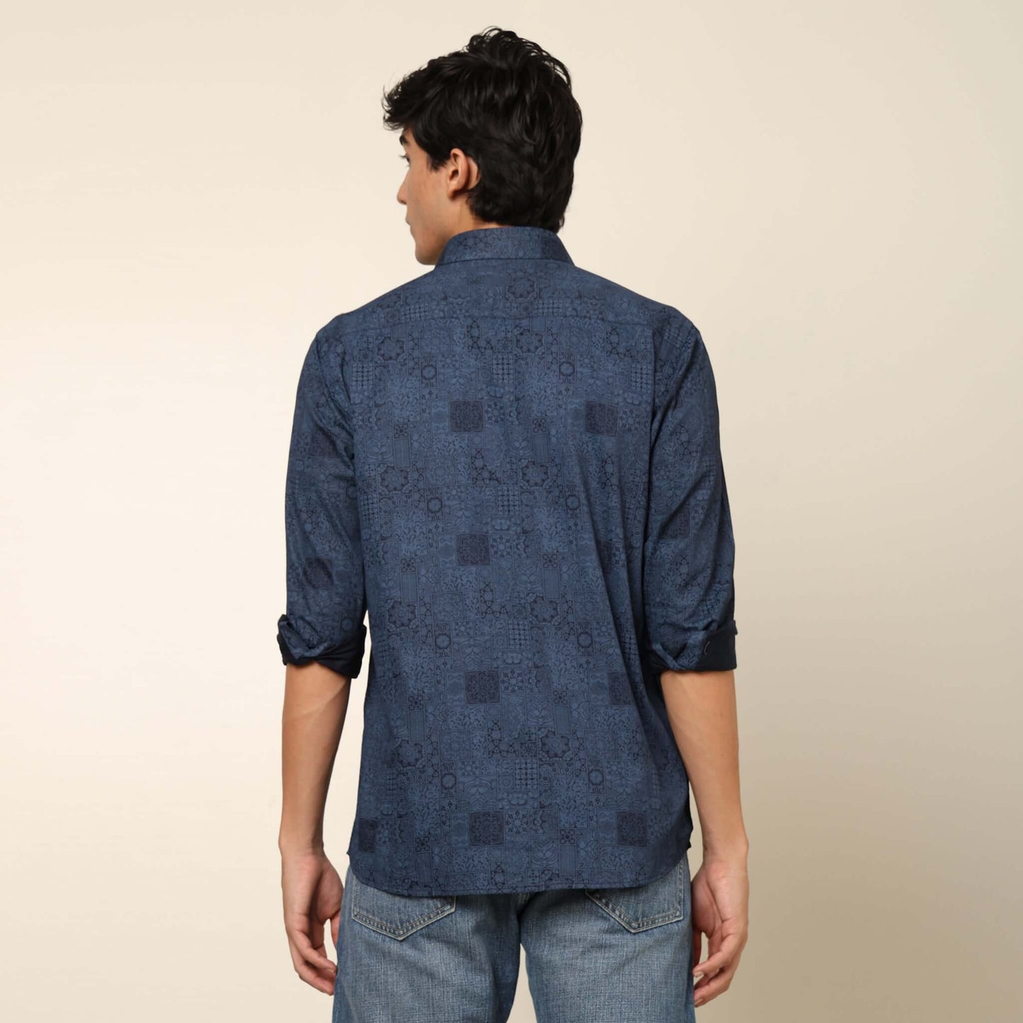 Model posing in regular fit printed blue casual shirt for men by Crease India, made up of soft cotton satin fabric it has floral and geometric prints along with long sleeves. Perfect for men to wear it as party shirt, brunch shirt, after party shirt, casu