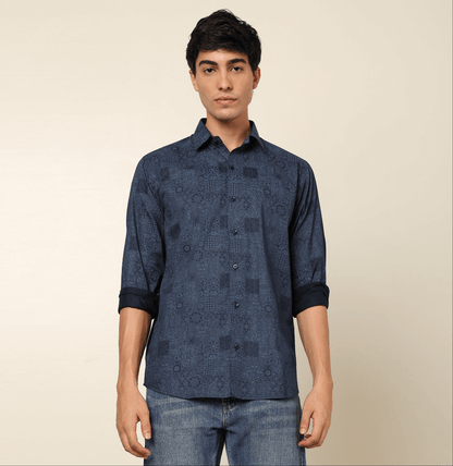 Model posing in regular fit printed blue casual shirt for men by Crease India, made up of soft cotton satin fabric it has floral and geometric prints along with long sleeves. Perfect for men to wear it as party shirt, brunch shirt, after party shirt, casu