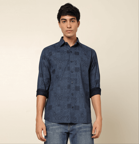 Model posing in regular fit printed blue casual shirt for men by Crease India, made up of soft cotton satin fabric it has floral and geometric prints along with long sleeves. Perfect for men to wear it as party shirt, brunch shirt, after party shirt, casu