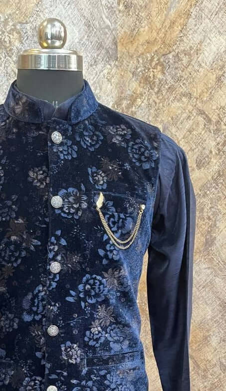 The Royal Blue Kurta jacket set for men is available online in India. The jacket is made with a velvet fabric with embossed floral patterns. It has a mandarin collar and goes with a matching blue hue dupion silk kurta & pants. This blue designer kurta set for men is perfect for weddings, parties, Diwali, Eid, Navratri & other traditional events. Shop this designer kurta jacket set for gents at the Crease India Website.